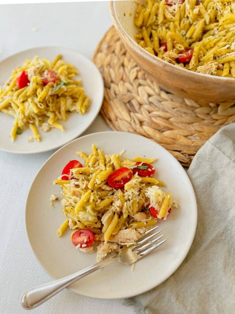 Plated pasta salad with pesto, chicken and tomatoes alongside a fork and napkin.