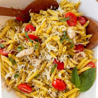 A large bowl of pesto chicken pasta salad garnished with a sprig of fresh basil.