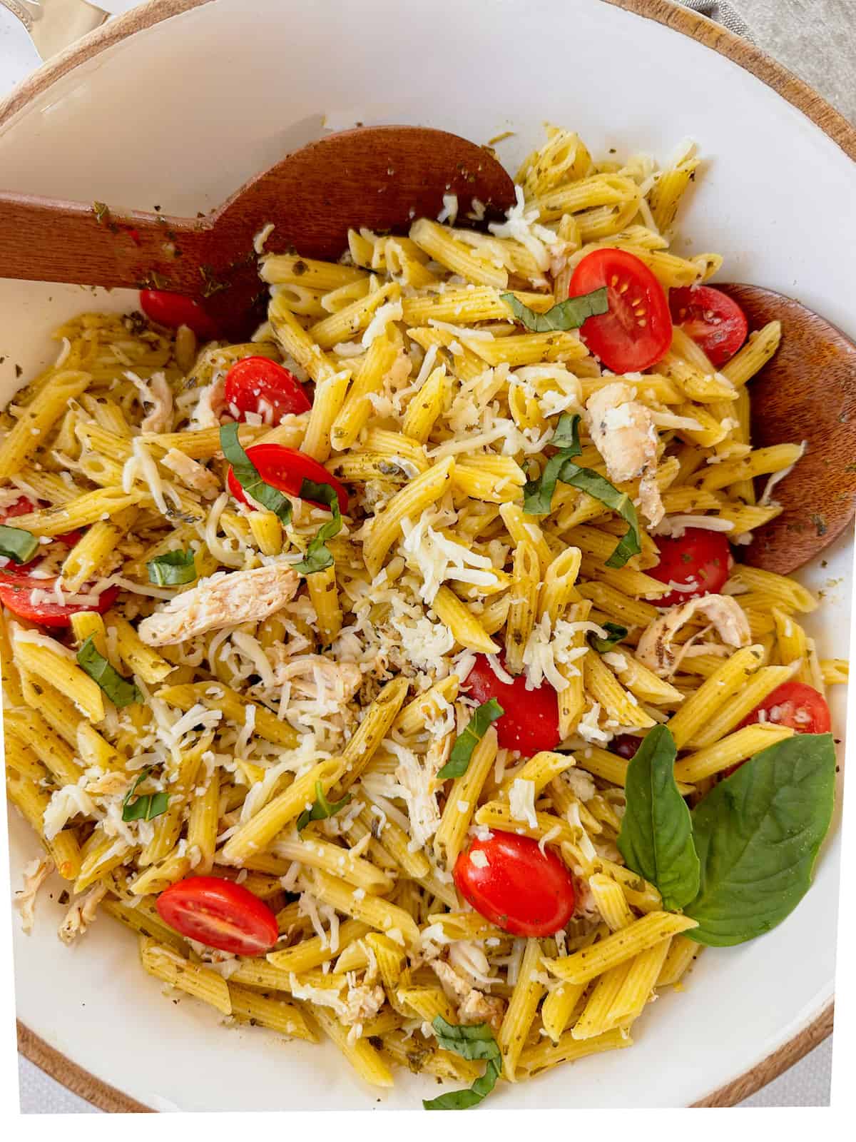 A large bowl of pesto chicken pasta salad garnished with a sprig of fresh basil.