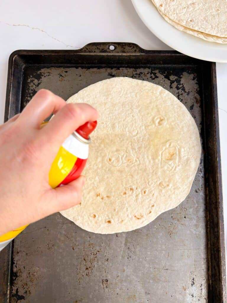 Spraying a large flour tortilla with nonstick cooking spray.