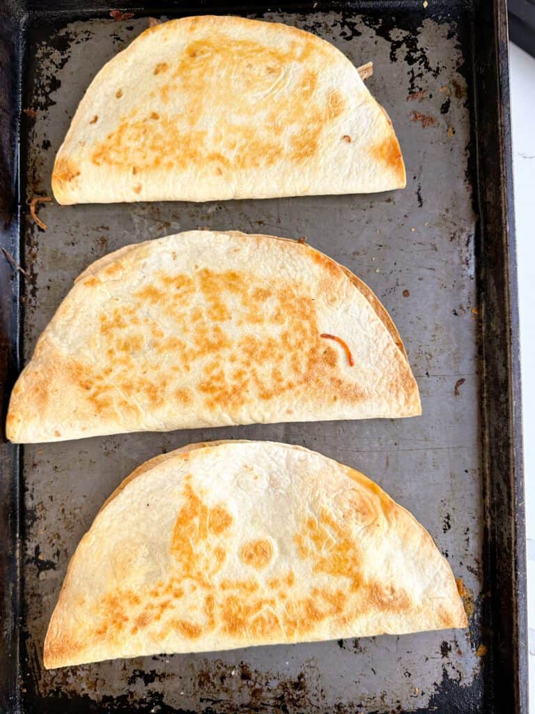 Three toasted quesadillas on a sheet pan.