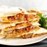 A stack of pulled pork quesadillas with bbq sauce and cheese.
