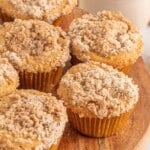 Crumb topped apple muffins on a wood platter.