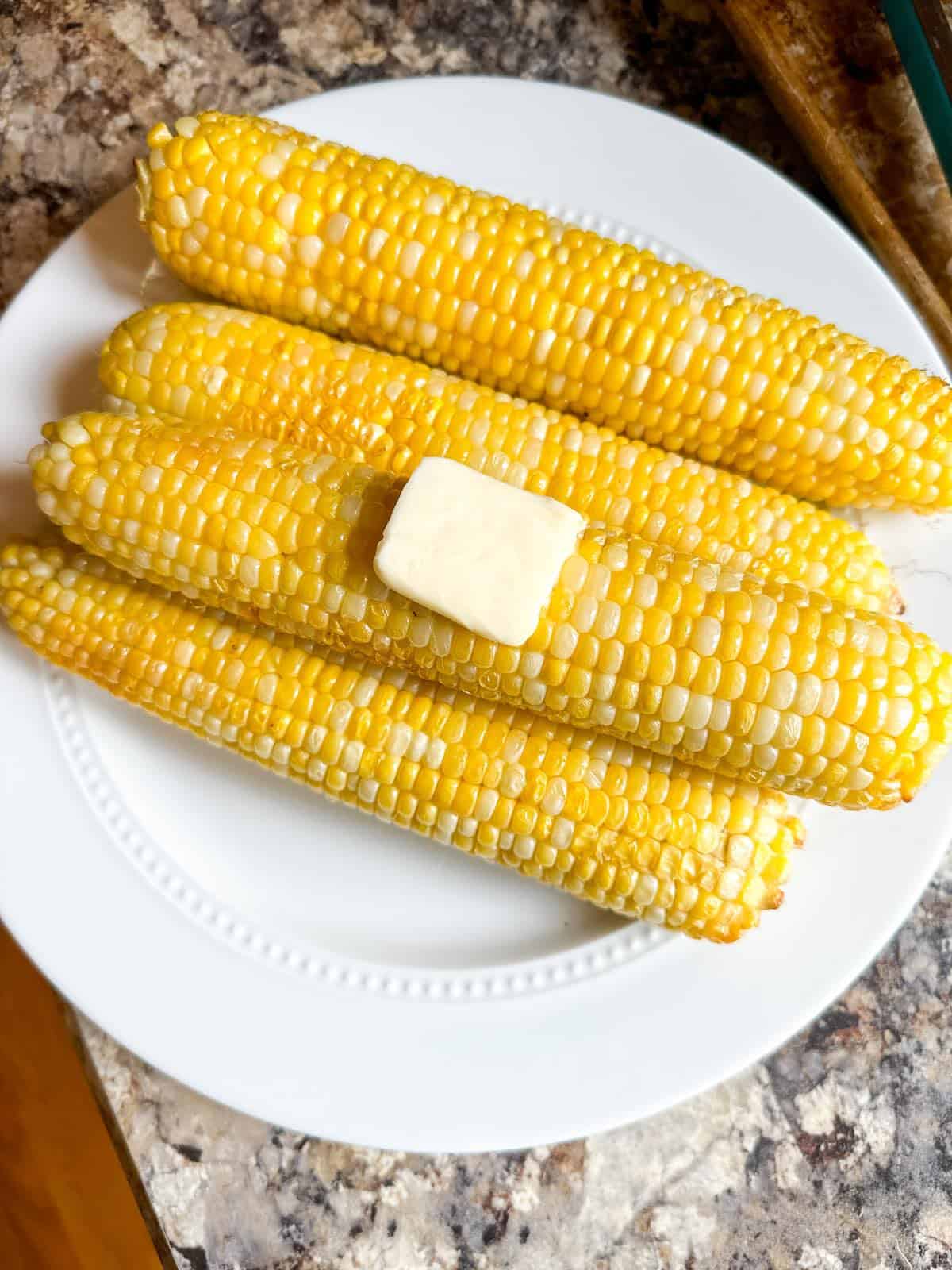 Cooked sweet corn on a plate topped with a pat of butter and seasoned with salt.