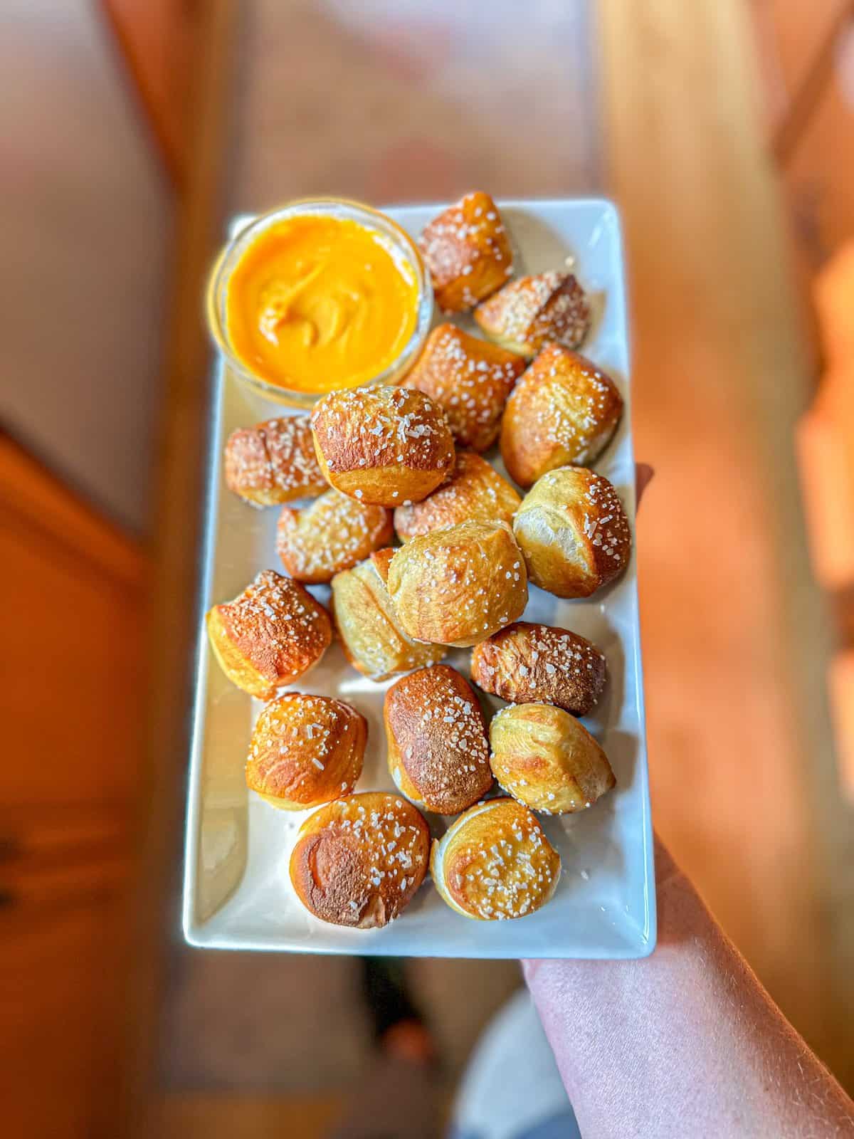 Plated pretzel bites sprinkled with salt on a white platter with a side of cheese.