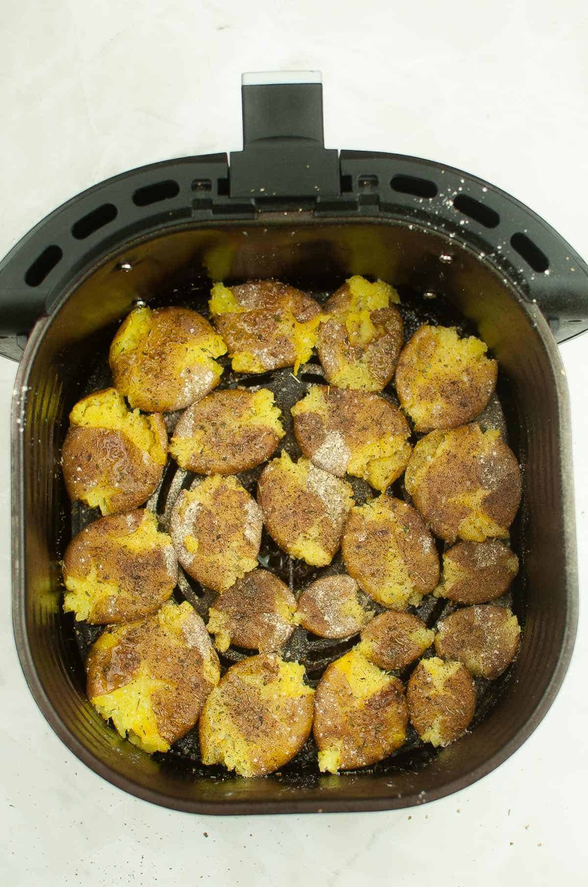 Smashed potatoes brushed with olive oil in an air fryer basket.