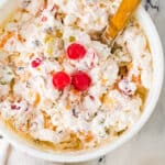 Ambrosia salad in a bowl with a wooden spoon topped with three cherries.