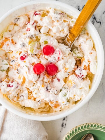 Ambrosia salad in a bowl with a wooden spoon topped with three cherries.