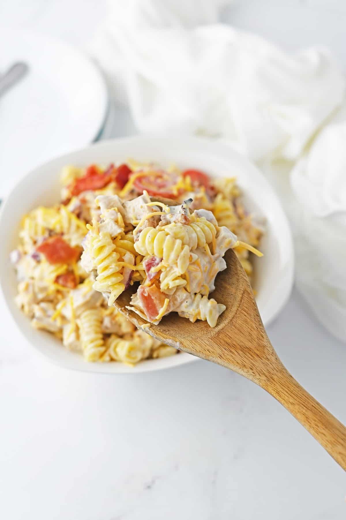 A spoonful of pasta salad with chicken, bacon and tomatoes.