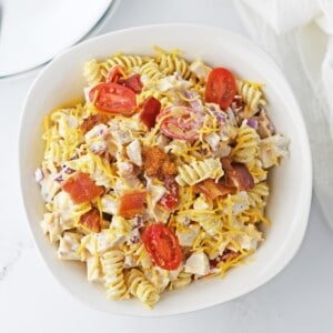 A bowl full of pasta salad topped with chicken, bacon, and tomatoes.