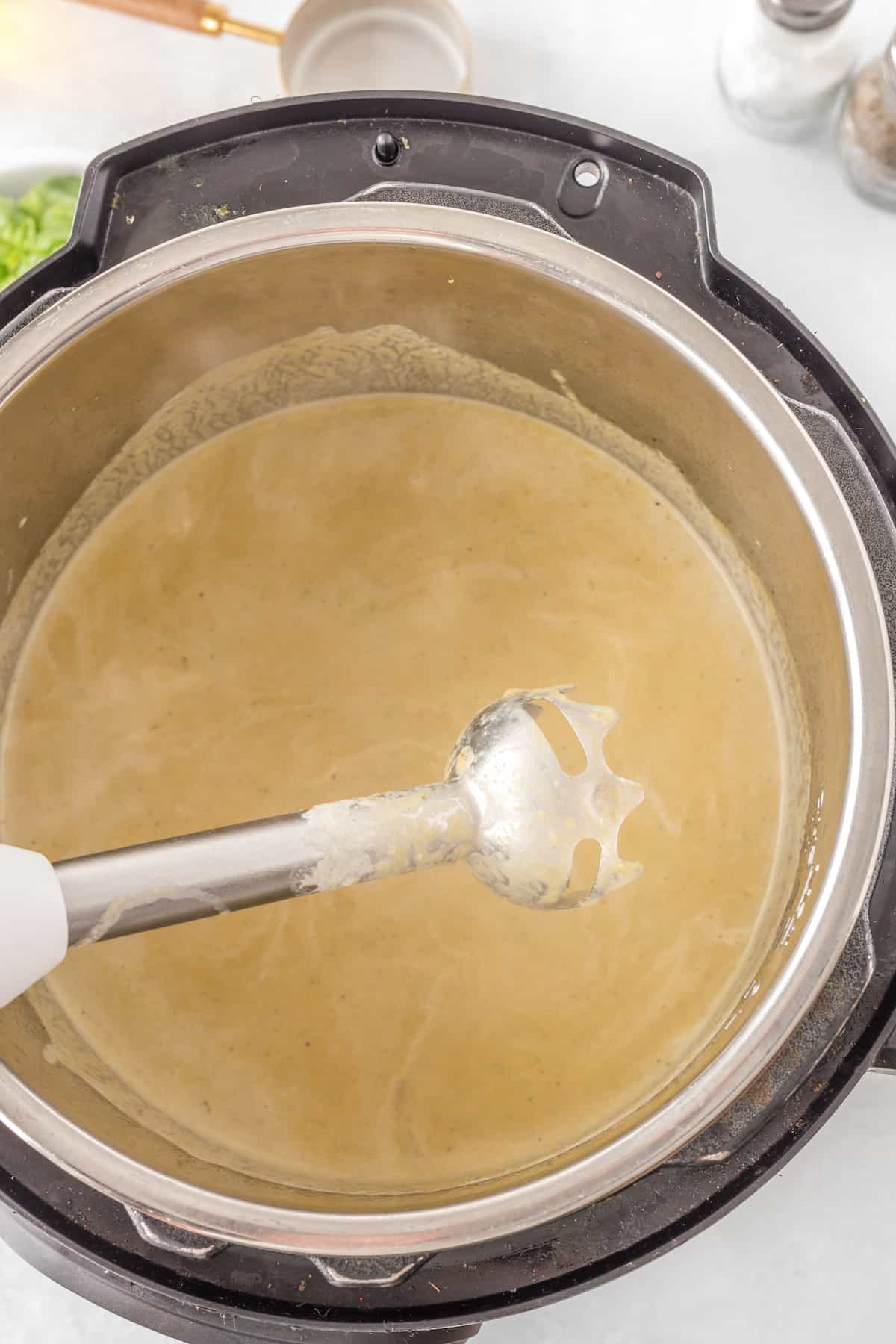 An immersion blender alongside the pot of  creamy instant pot asparagus soup.