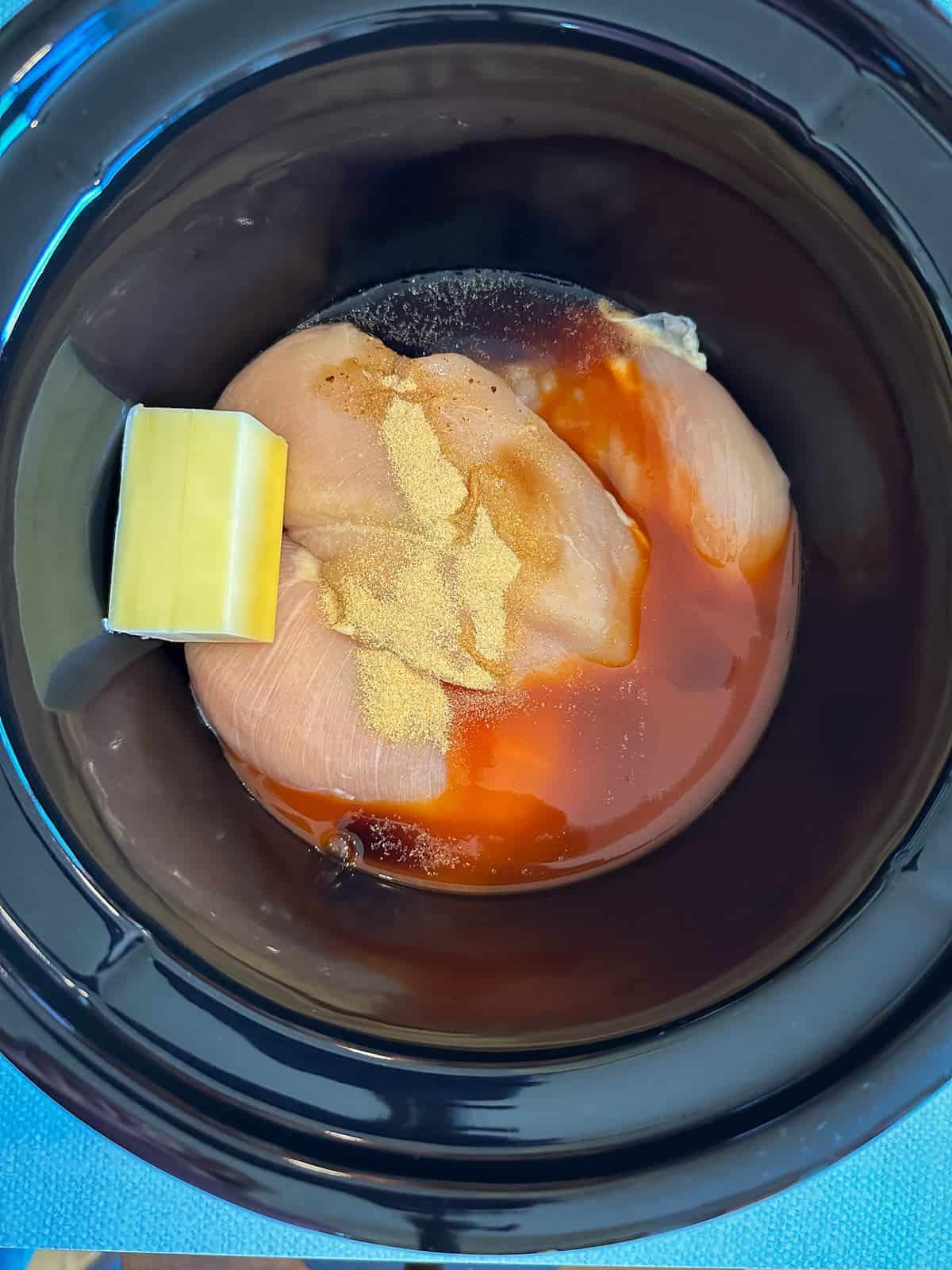 Chicken breasts with butter and hot sauce in a crockpot.