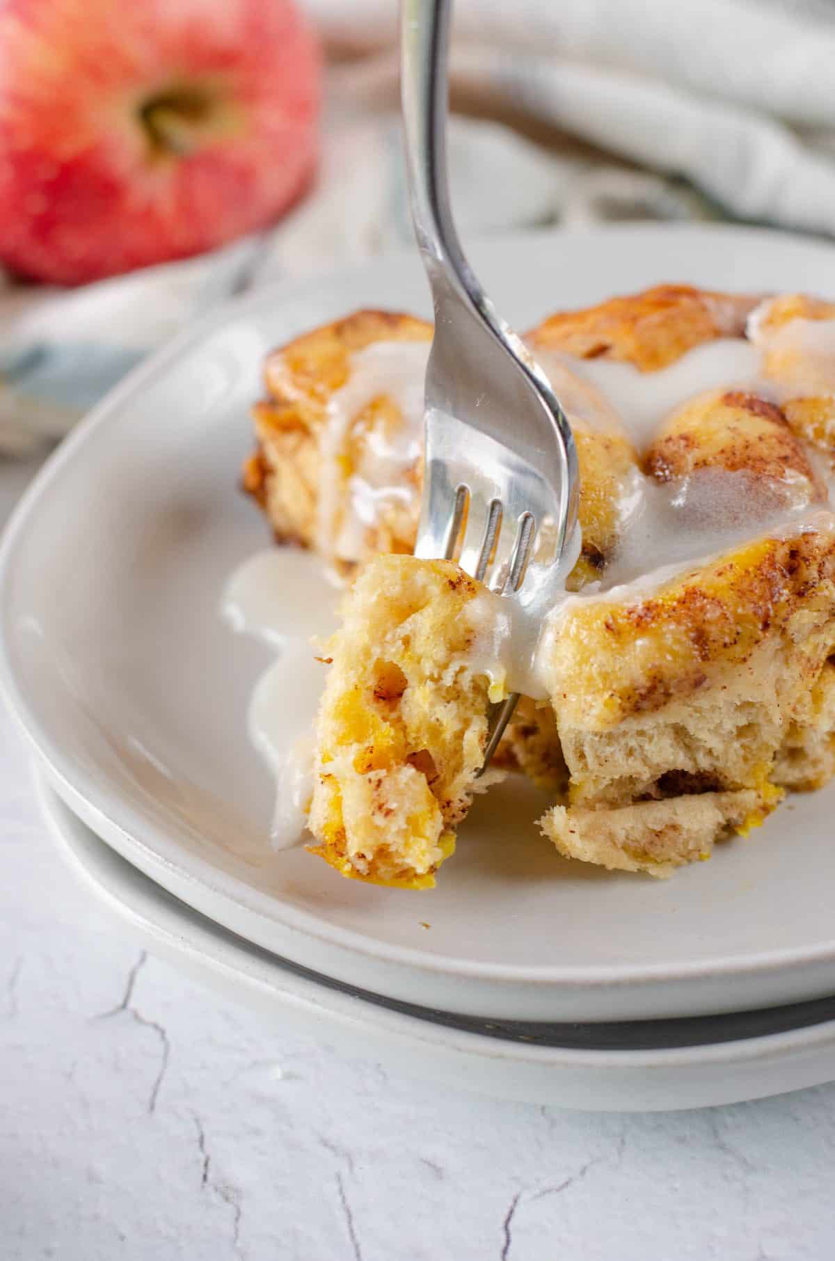 A forkful of cinnamon roll on a plate with icing dripping down the sides.