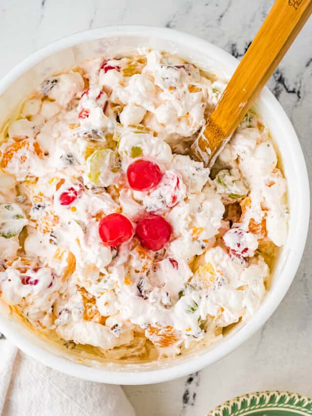Ambrosia salad in a bowl with a wooden spoon topped with three cherries.