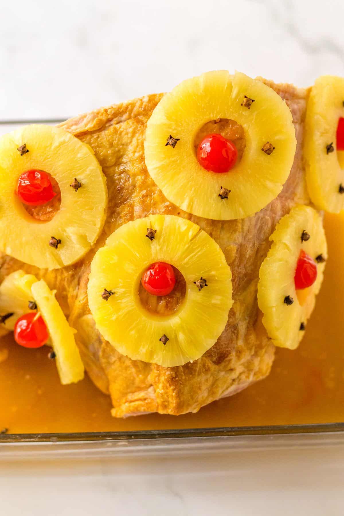 Pineapple and cherry topped ham in a baking dish.