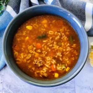 A bowl of hamburger vegetable soup with alphabet pasta floating on top.