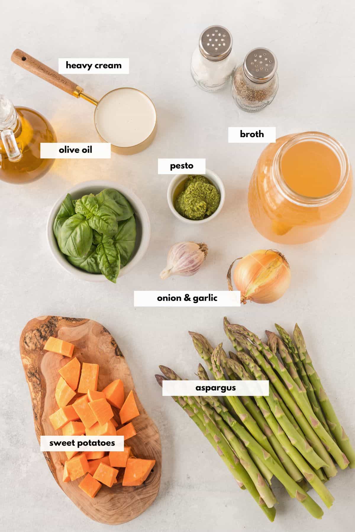 Ingredients for a healthier asparagus soup including sweet potatoes, broth, pesto, olive oil, garlic, onion and heavy cream.