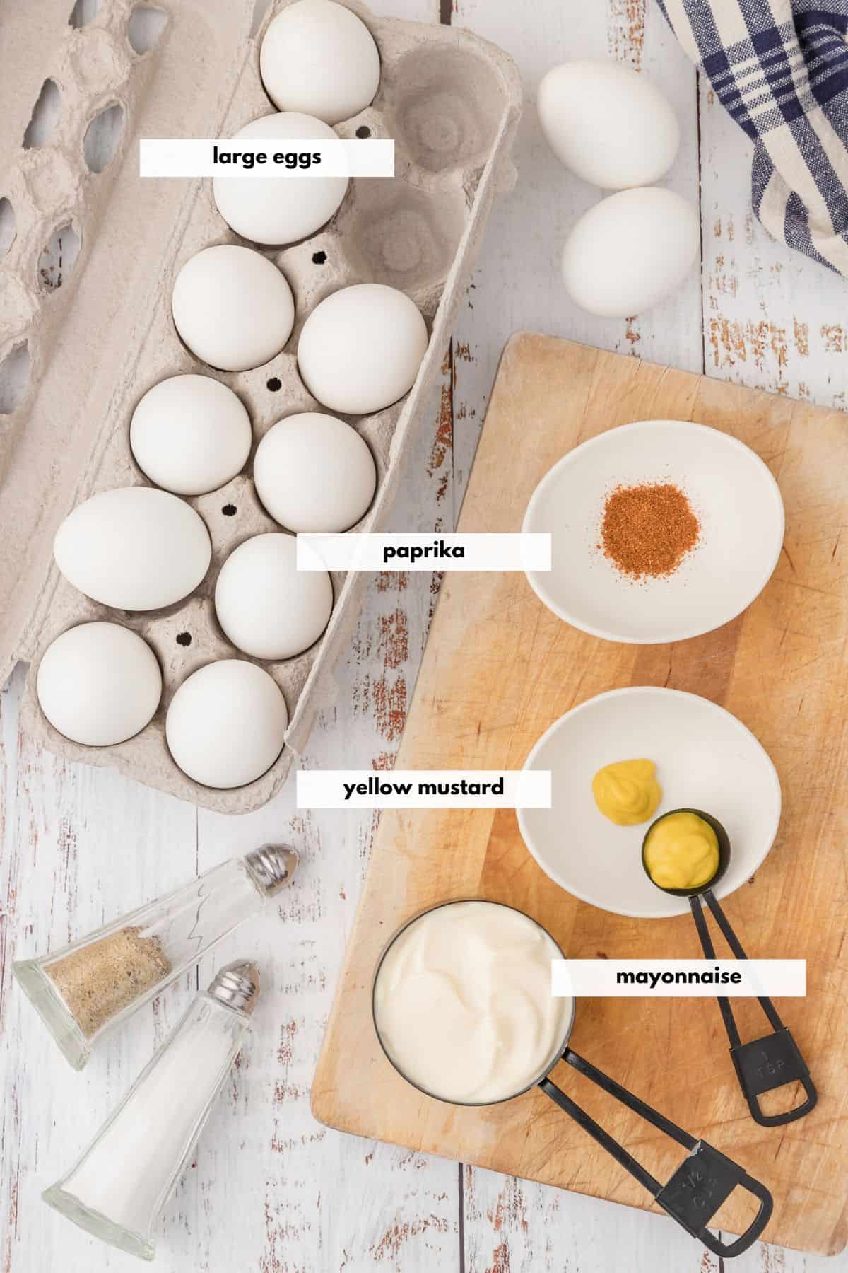 Ingredients to make deviled eggs including mayonnaise, yellow mustard, paprika, eggs, salt and pepper.