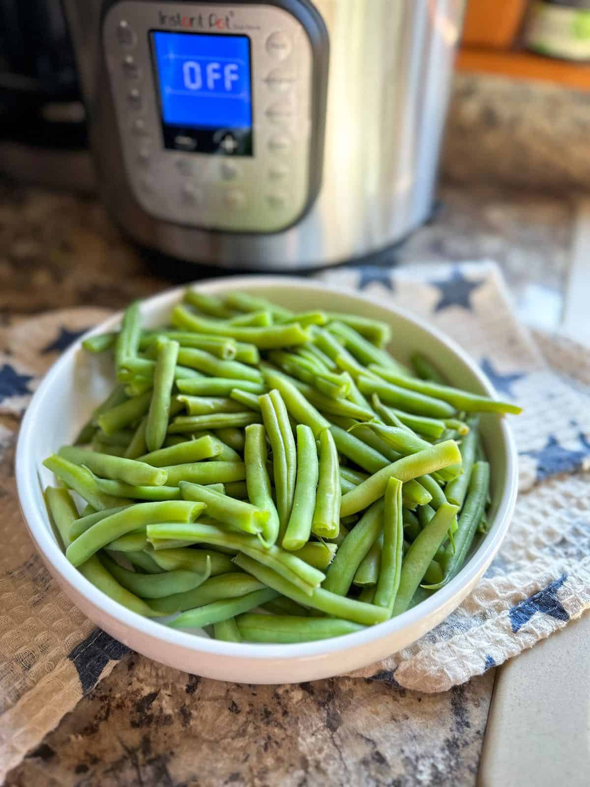 A bowl of green beans next to an Instant Pot.