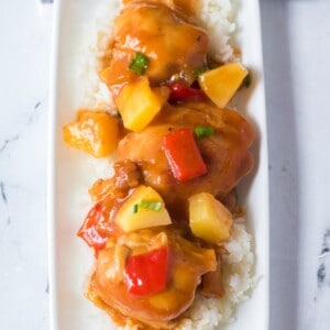 Plated pineapple and red bell pepper chicken on a bed of rice.