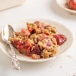A plate full of baked strawberries with an oatmeal topping and a spoon.
