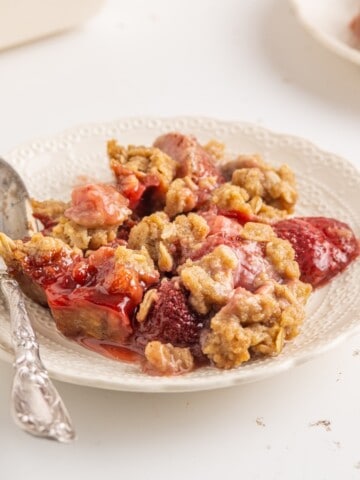 A plate full of baked strawberries with an oatmeal topping and a spoon.