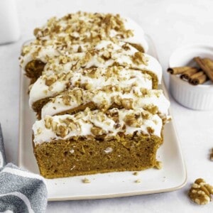 Cream cheese and walnut topped slices of pumpkin bread on a rectangle platter.