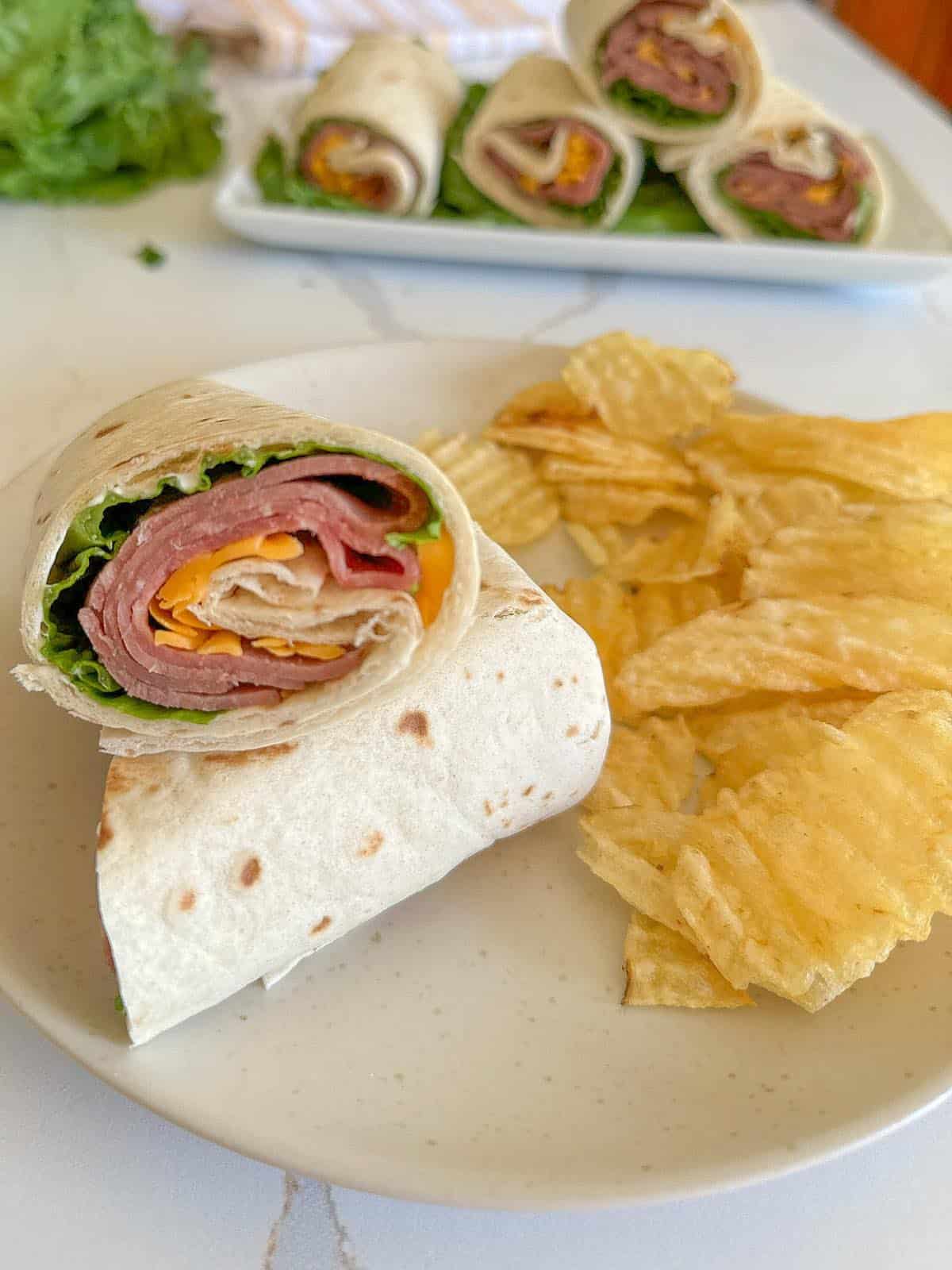 A plated roast beef wrap with potato chips on the side.