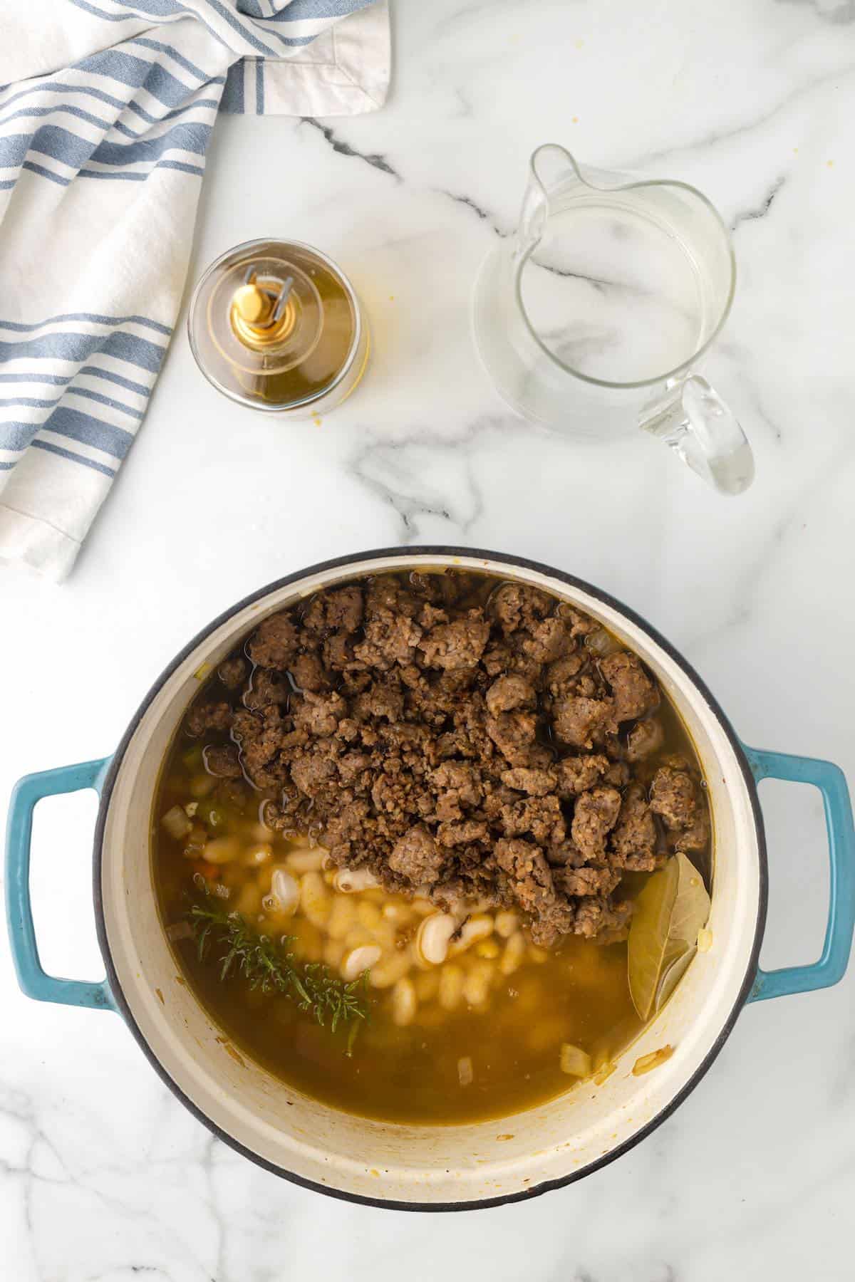 Italian sausage, chicken broth and white beans in a pot.