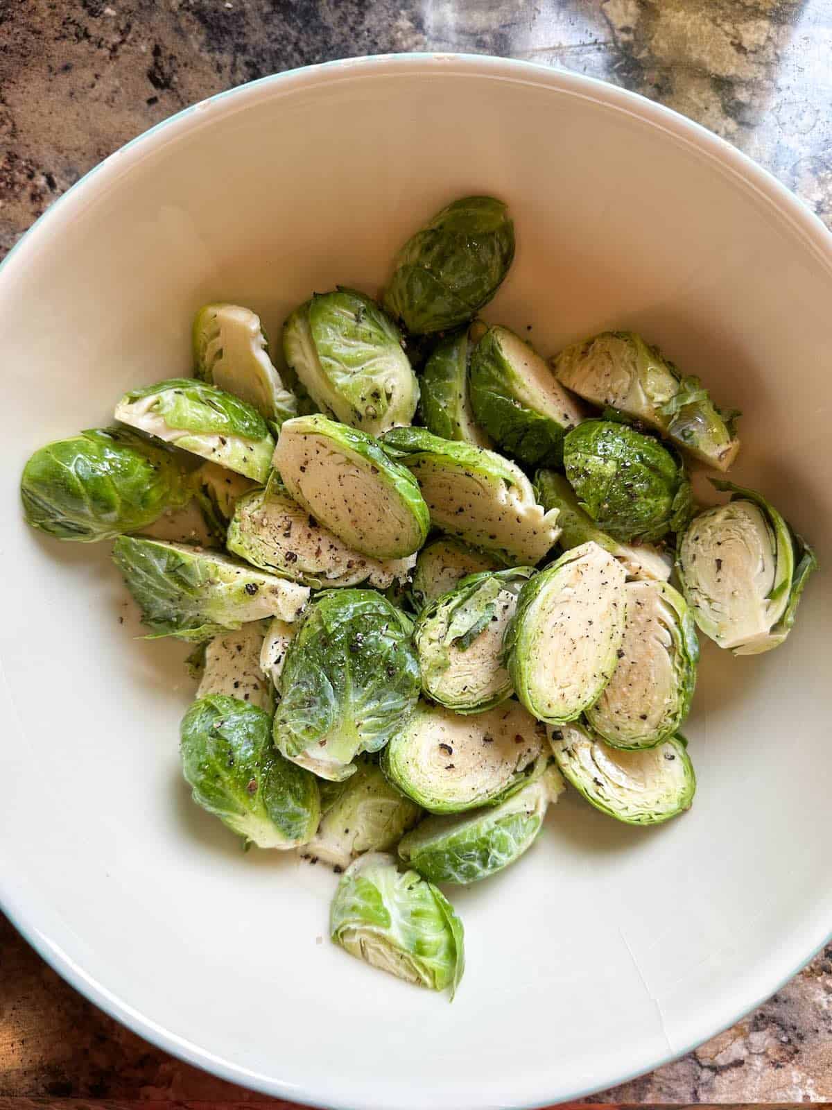 Brussels sprouts tossed in extra virgin olive oil, salt and pepper in a bowl.