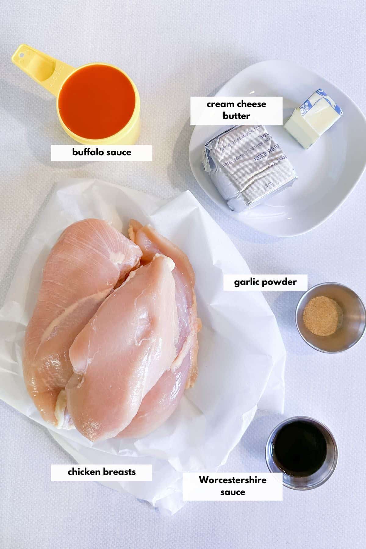 Ingredients to make pulled buffalo chicken including chicken breasts, buffalo sauce, cream cheese, butter, garlic powder and Worcestershire sauce.