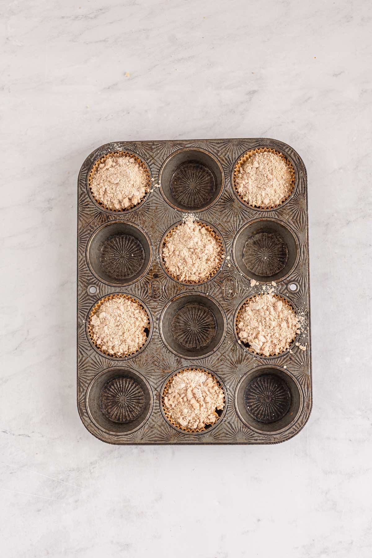 Portioned muffins in a muffin tin, topped by a spiced crumb topping.