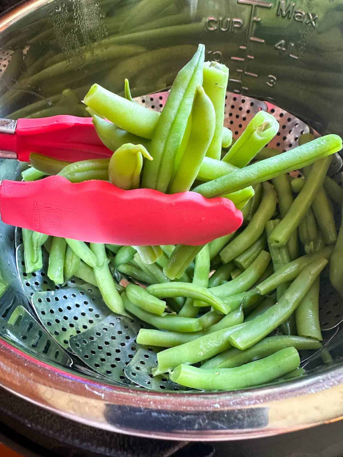 Red tongs holding cooked green beans.