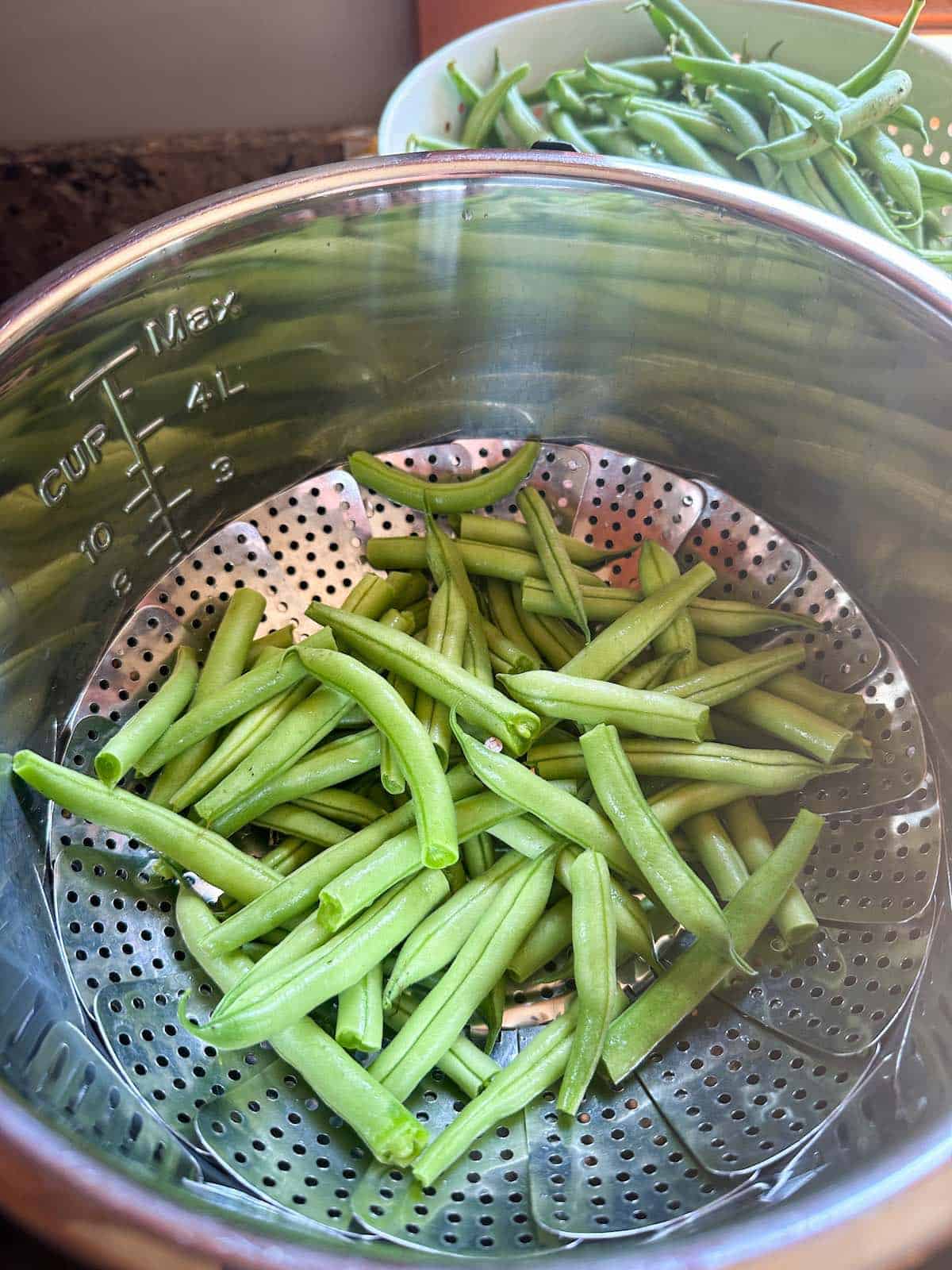 A steamer basket with cut green beans in it.