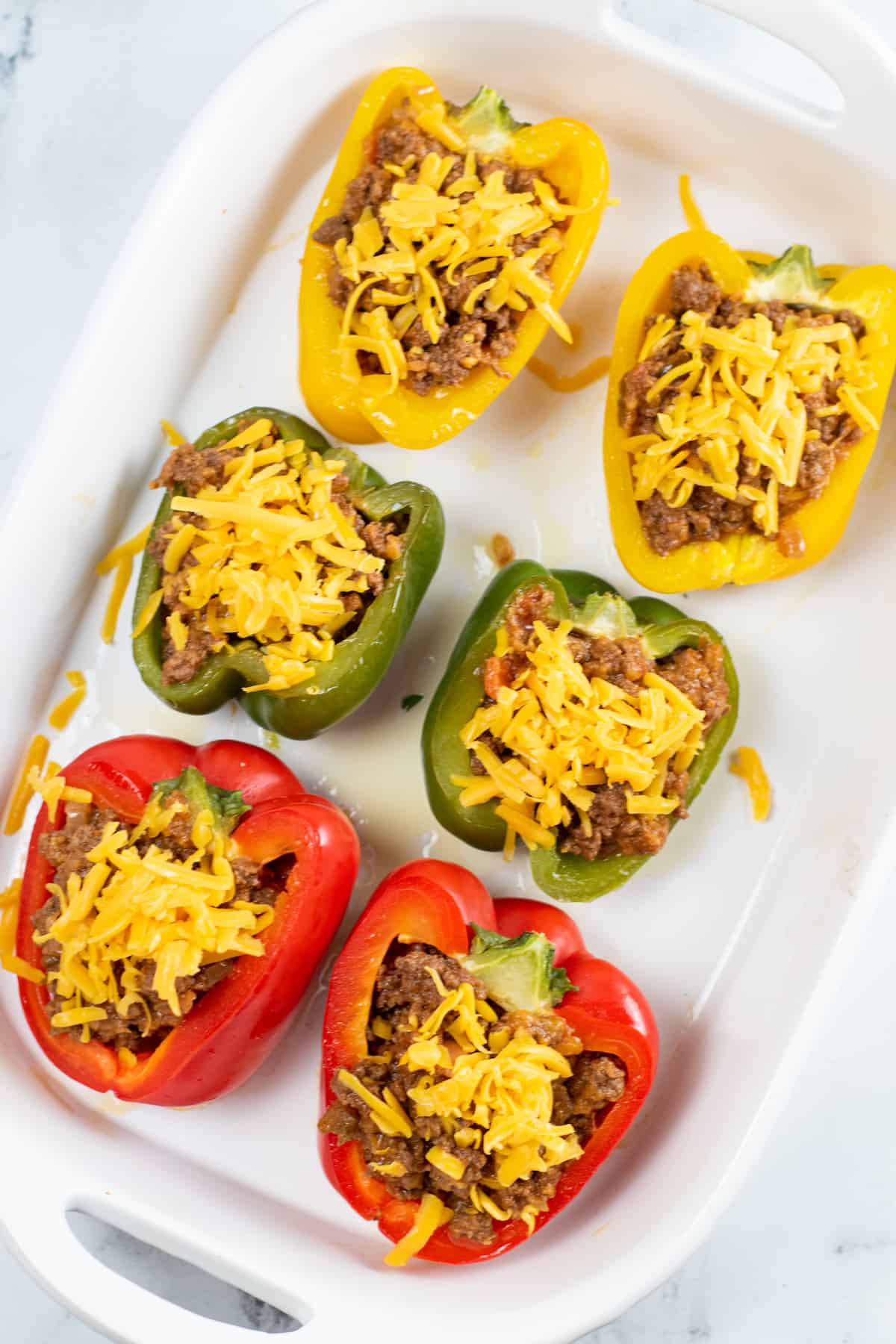 Stuffed pepper halves topped with cheddar cheese in a baking dish.