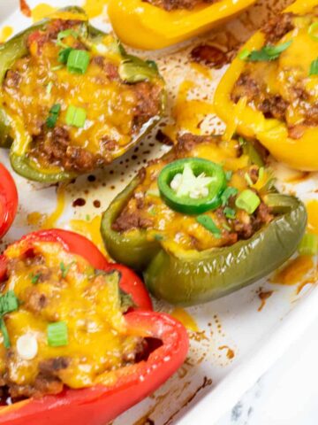 Stuffed taco peppers in a casserole dish topped with melted cheese and a jalapeno slice.