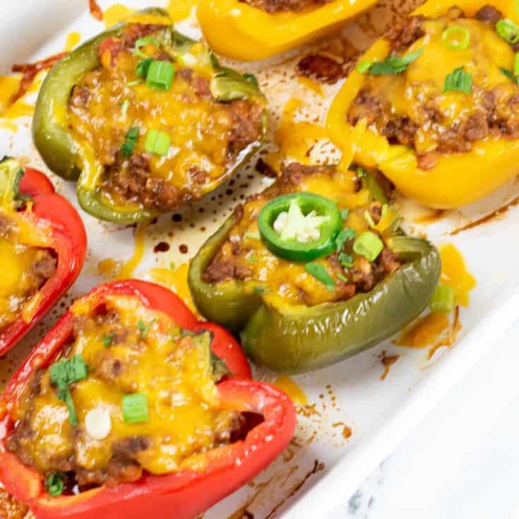 Stuffed taco peppers in a casserole dish topped with melted cheese and a jalapeno slice.