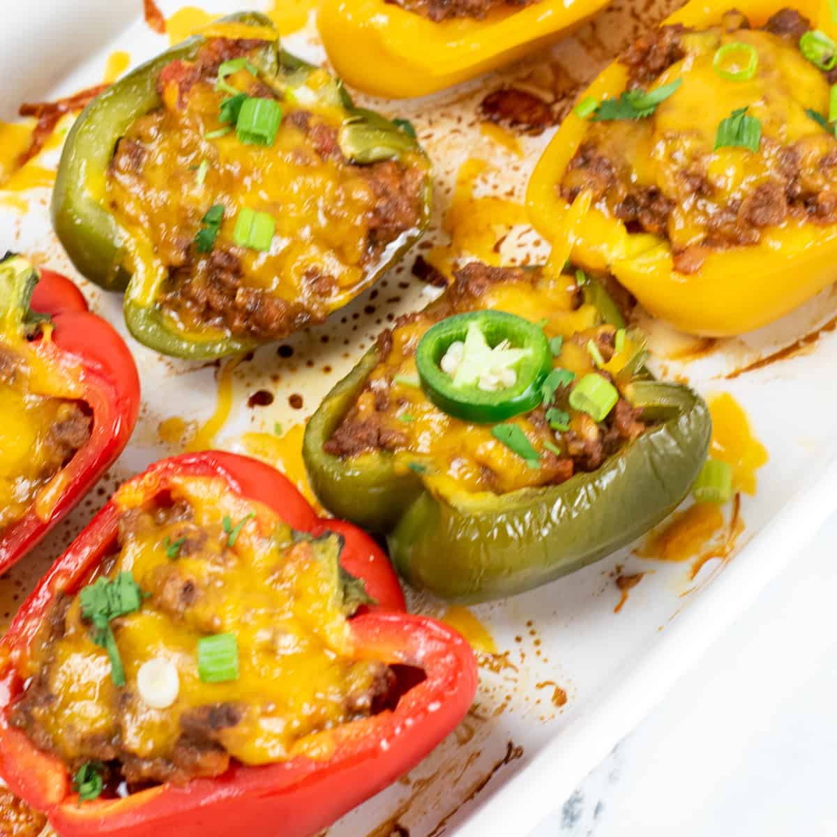 Stuffed taco peppers in a casserole dish topped with melted cheese and a jalapeno slice.