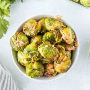 A bowl full of air fried brussels sprouts with shredded parmesan cheese.