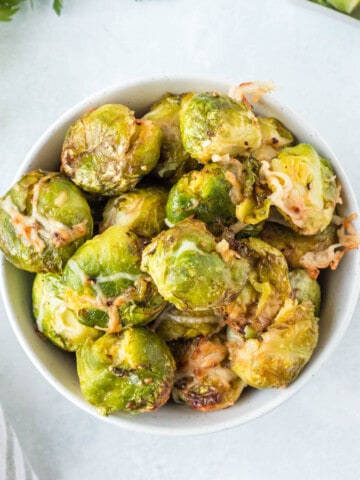 A bowl full of air fried brussels sprouts with shredded parmesan cheese.