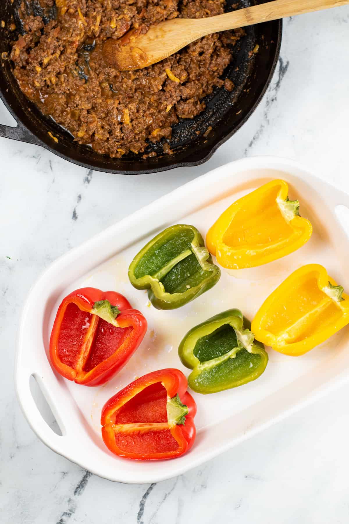 Red, yellow and green bell pepper halves in a baking pan.