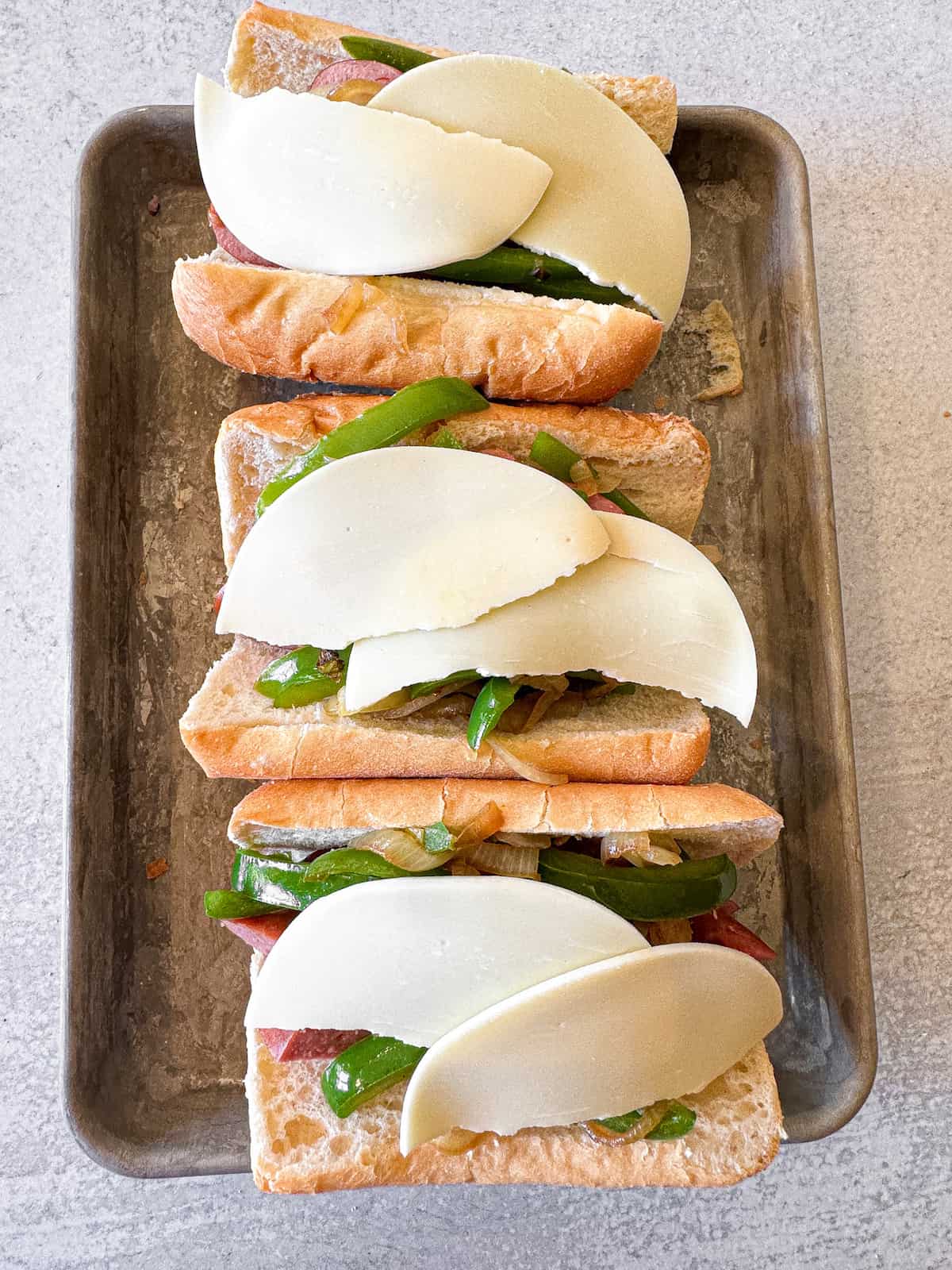 Cheesy sausage sandwiches on a baking pan.