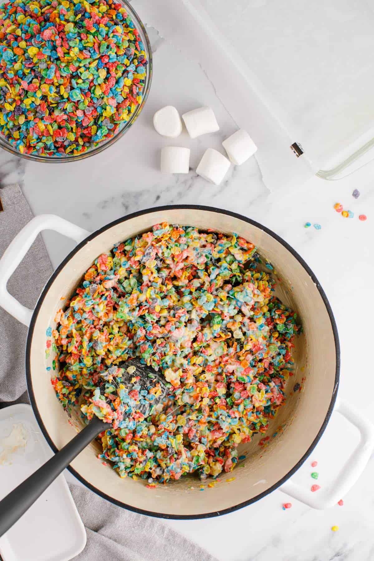 A large saucepan with melted marshmallows and cereal combined with a spoon.