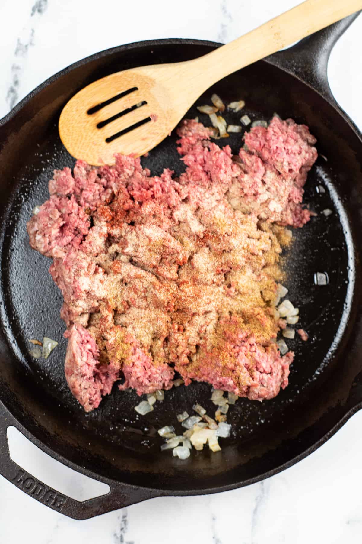 Ground beef and onions in a cast iron skillet with a wooden spoon.
