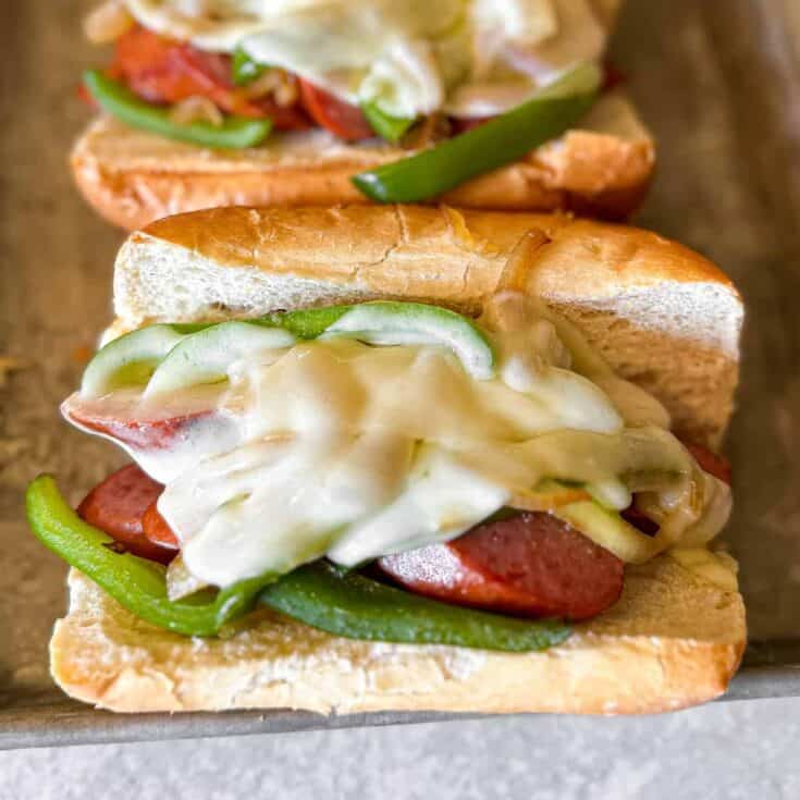 Peppers and onions on grilled kielbasa sandwiches topped with cheese.