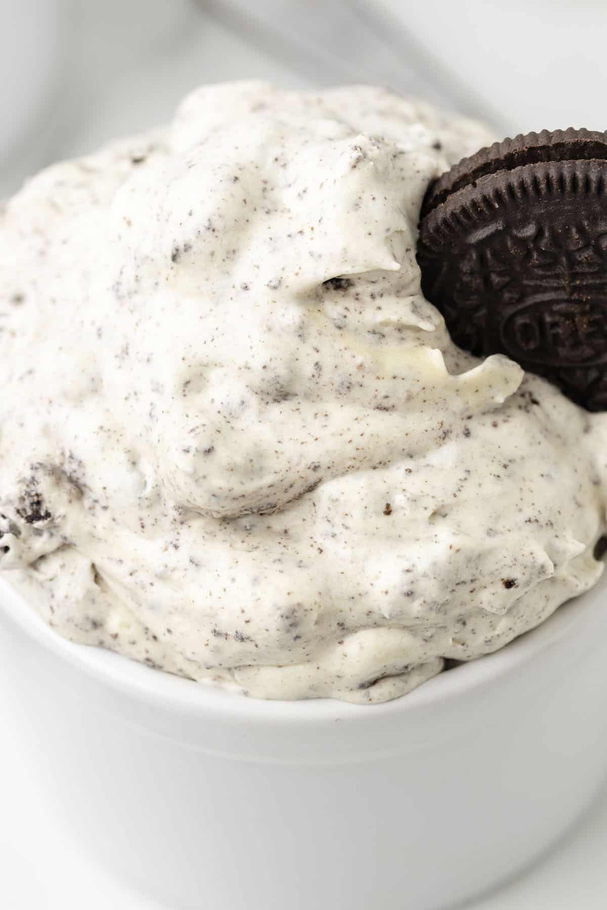 A fluffy bowl of cookies and cream dessert topped with an oreo cookie.