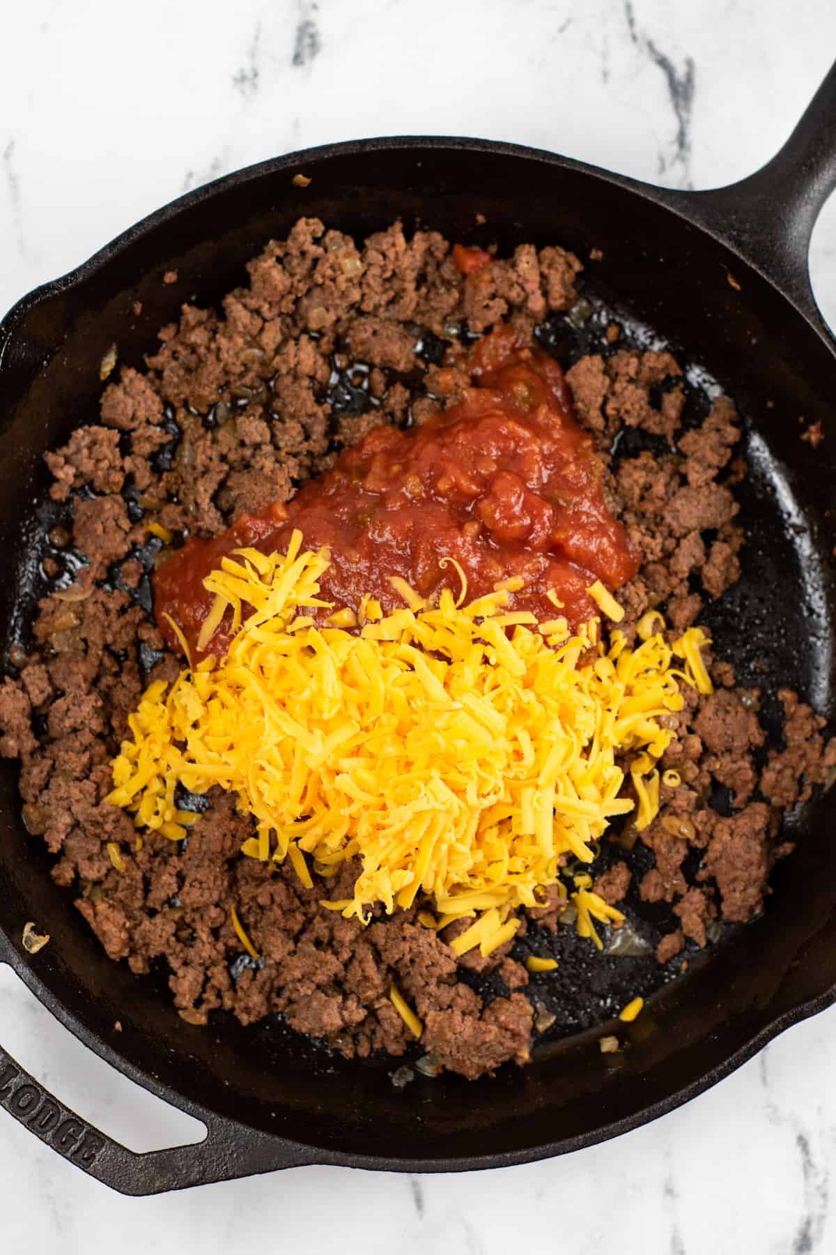 Seasoned and cooked ground beef in a skillet topped with shredded cheese and salsa.