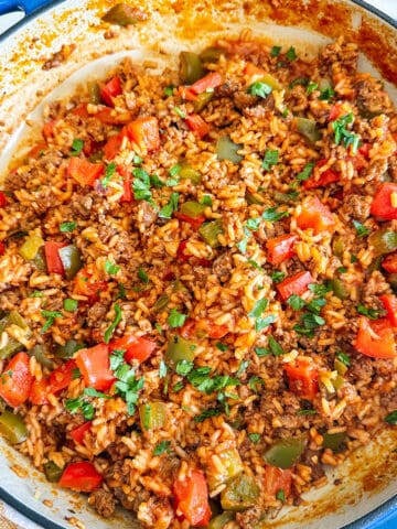 Ground beef, bell peppers, rice and tomato sauce in a blue enamel skillet.