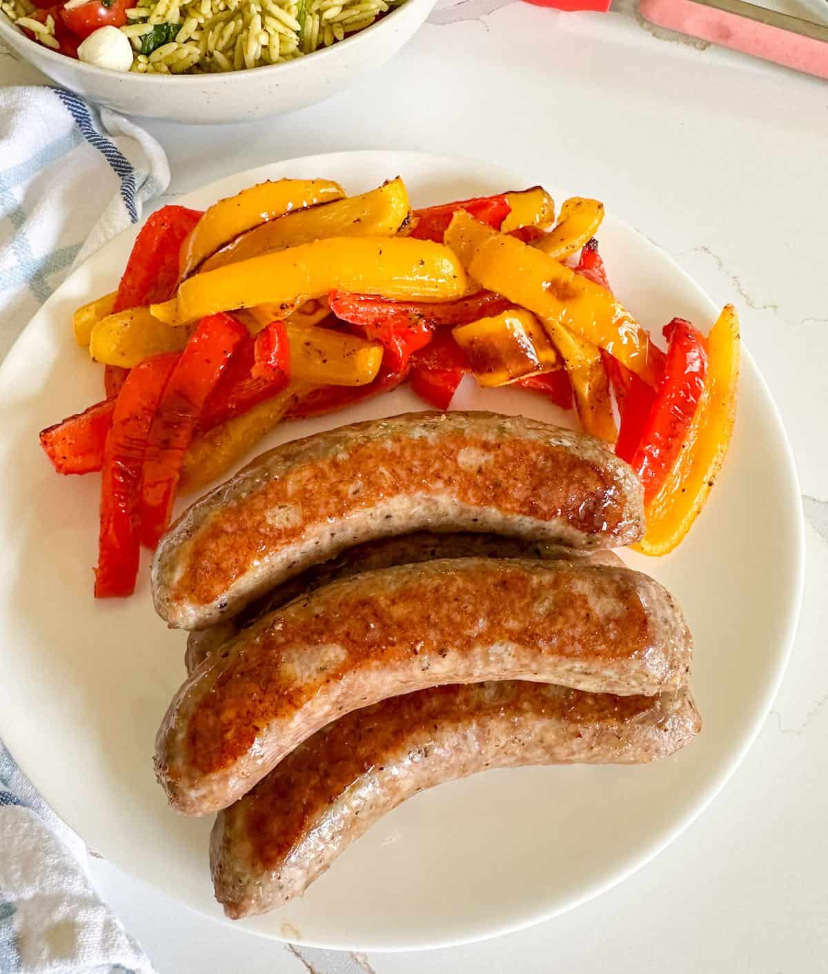 Cooked baked Italian sausages and peppers on a white dinner plate.