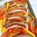 Baked Italian sausages on a baking sheet with cooked bell peppers.